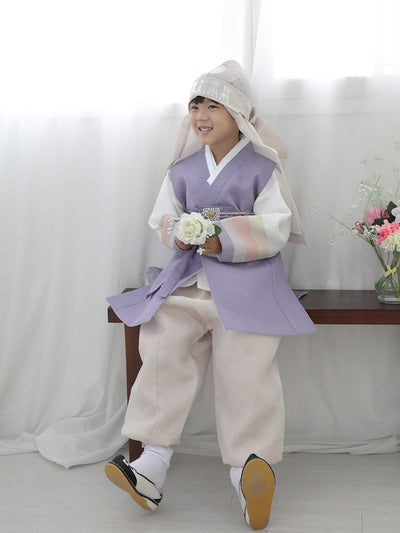 우리의 Spring Boys Hanbok in Pastel Lavender를 입고 편안하게 웃으며 앉아있는 소년